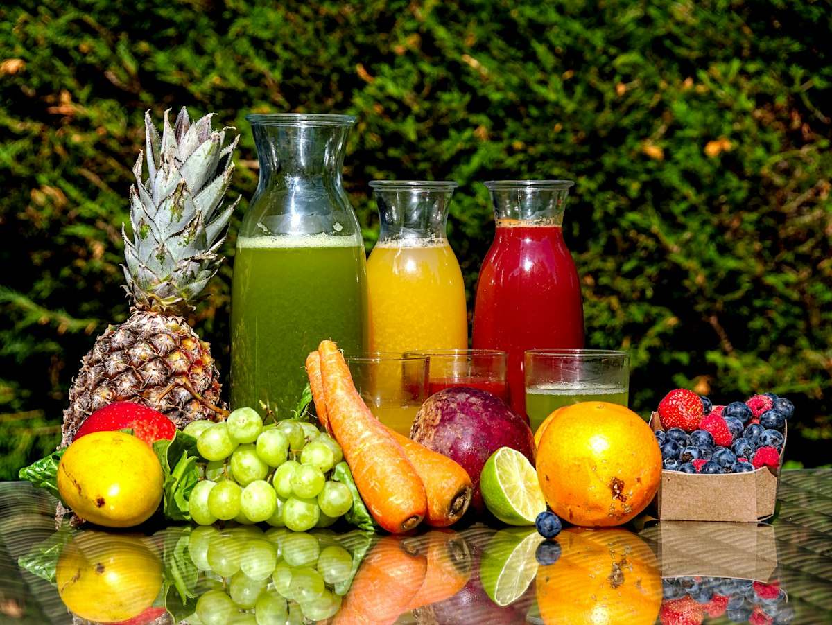 Garrafas de suco natural ao lado de abacaxi, uvas, cenoura, laranja e frutas vermelhas