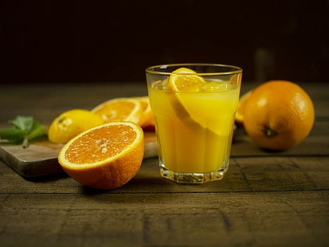 Suco de laranja natural em copo de vidro com laranjas ao lado